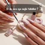 Billedet viser en elegant scene med hænder, der arbejder med neglekunst i bløde, feminine nuancer af rosa og guld. En pensel påfører lak på en negl, mens omgivelserne fremhæver professionelle negleværktøjer og fine detaljer. Stemningen er rolig og luksuriøs med fokus på præcision og skønhed. Dette billede illustrerer muligheden for at blive en del af BeautyByDau som negletekniker og afspejler vores brand’s feminine og kvalitetsbevidste univers. Perfekt til dig, der brænder for neglekunst og ønsker en arbejdsplads med hjerte og kvalitet.