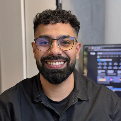 Amir, co-founder og Head of Marketing hos BeautyByDau, smiler foran skærm med mørk skjorte og briller.